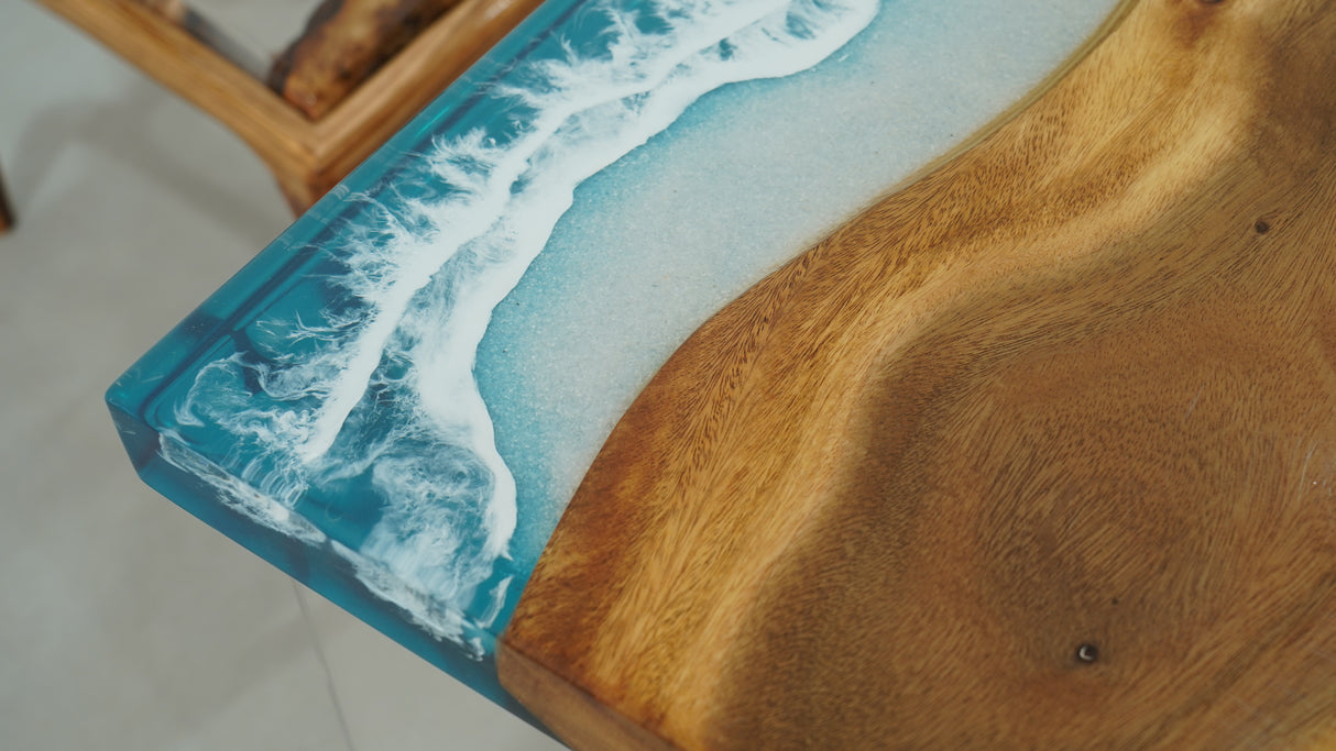 A straight-edge resin table with a natural wood grain pattern merging into a blue resin section resembling ocean waves