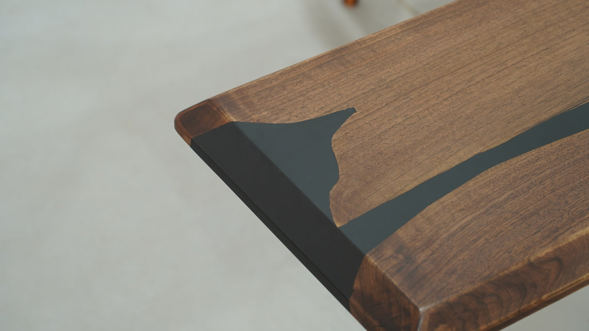 A long straight-edge dining or coffee table made of wood with black resin inlays, accompanied by a uniquely designed wooden chair with resin details