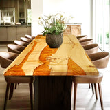 Rectangular epoxy - resin and wood dining table with a striking orange resin inlay, adorned with a plant centerpiece and surrounded by brown leather chairs.