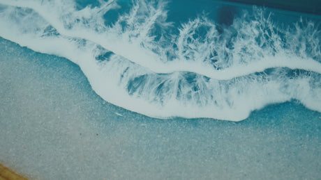 A stunning straight-edge resin table with a natural wood grain pattern merging into a blue resin section resembling ocean waves