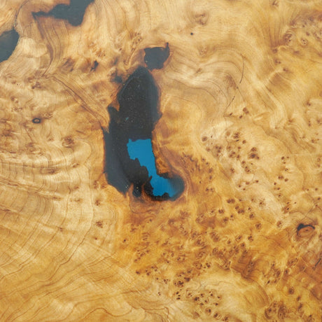 Close - up of a wooden tabletop with intricate patterns and an inlaid section of blue and black epoxy resin.