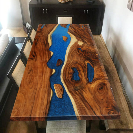 Rectangular wooden dining table with a striking blue epoxy - resin river - like inlay, surrounded by chairs in a home setting.