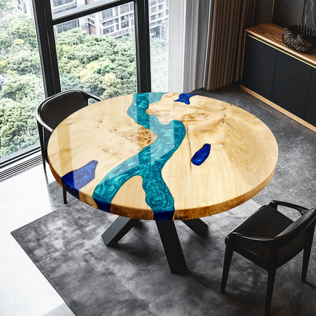 Round epoxy - resin and wood table with blue resin inlay, placed in a modern room with large windows, a rug, and black chairs.