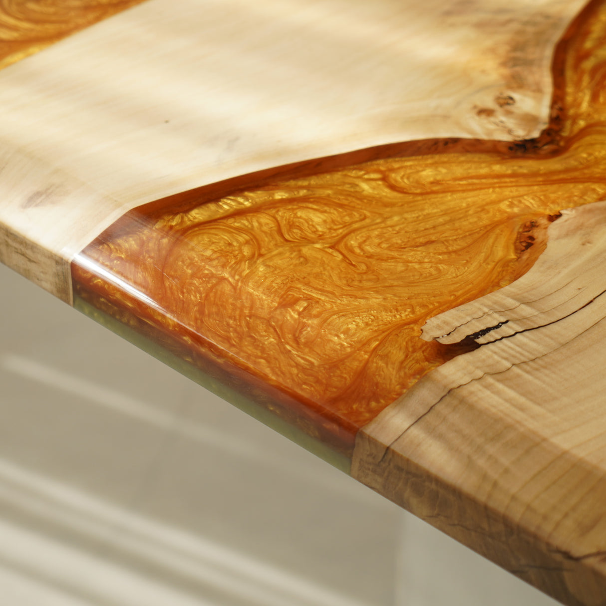 Close - up of a wooden tabletop with an inlaid section of swirling orange epoxy resin, showcasing the seamless blend of materials.