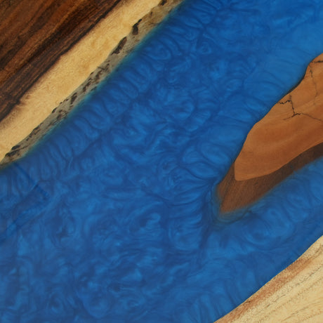 Close - up of a blue epoxy - resin inlay on a wooden tabletop, highlighting the resin's swirling patterns.