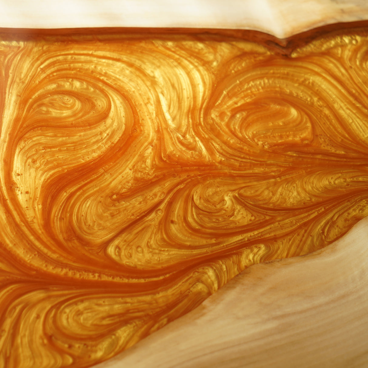 Close - up of an epoxy - resin pattern on a tabletop, featuring swirling orange and gold hues.
