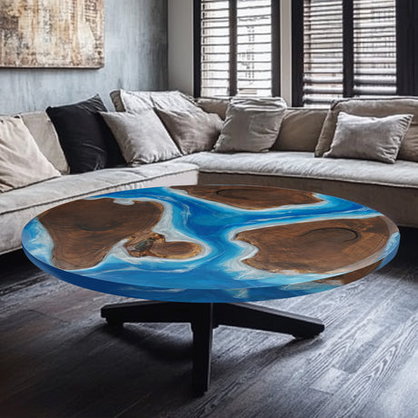 Round epoxy - resin and wood coffee table with a blue resin inlay, set against a backdrop of a sofa with cushions.
