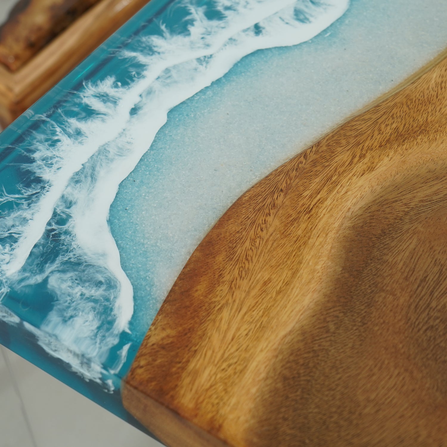 A straight-edge resin table with a natural wood grain pattern merging into a blue resin section resembling ocean waves