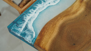 A straight-edge resin table with a natural wood grain pattern merging into a blue resin section resembling ocean waves