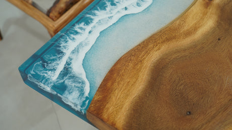 A straight-edge resin table with a natural wood grain pattern merging into a blue resin section resembling ocean waves
