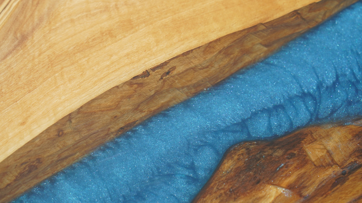 A wooden live-edge walnut table crafted from natural wood, featuring a striking blue epoxy-resin inlay, accompanied by a uniquely designed wooden chair with resin details.