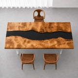 Handcrafted golden camphor wood dining table featuring a bold black epoxy resin river, intricate burl wood grain, and warm golden tones