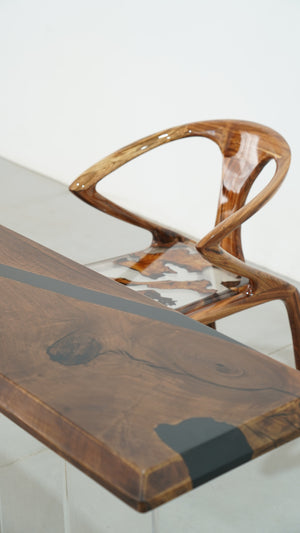 A long straight-edge dining or coffee table made of wood with black resin inlays, accompanied by a uniquely designed wooden chair with resin details