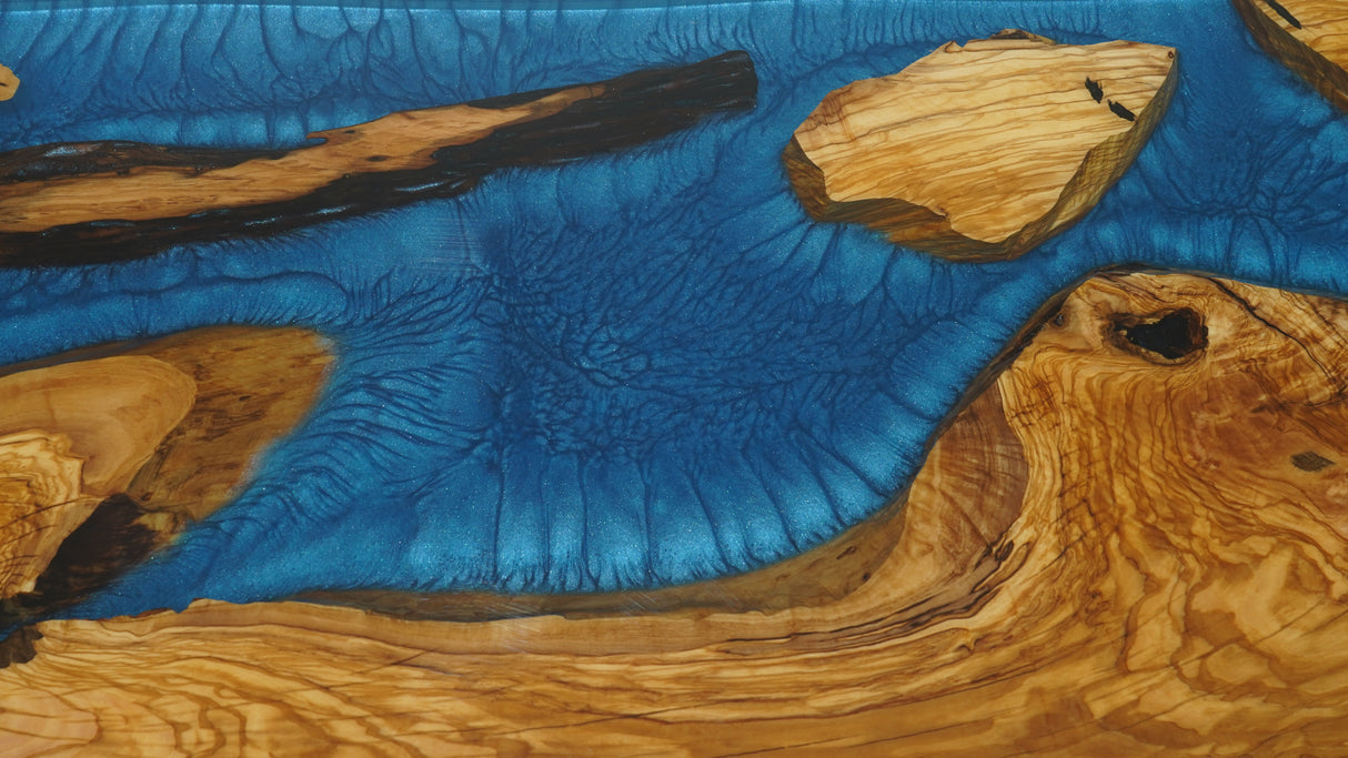 A custom live-edge walnut dinner table crafted from natural wood, featuring a striking blue epoxy-resin inlay, accompanied by a uniquely designed wooden chair with resin details.
